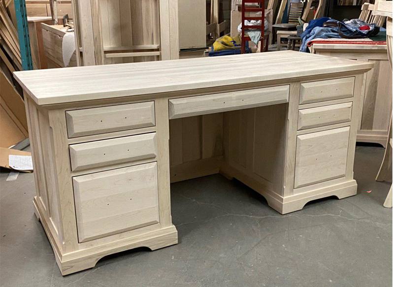 Large Unfinished Furniture Office Desk Made Of Light-Toned Solid Wood, Featuring Multiple Drawers And A Classic Design, Ready For Custom Finishing In A Workshop Setting.