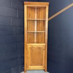 Tall wooden corner cabinet featuring open display shelves on top and a lower cupboard door.